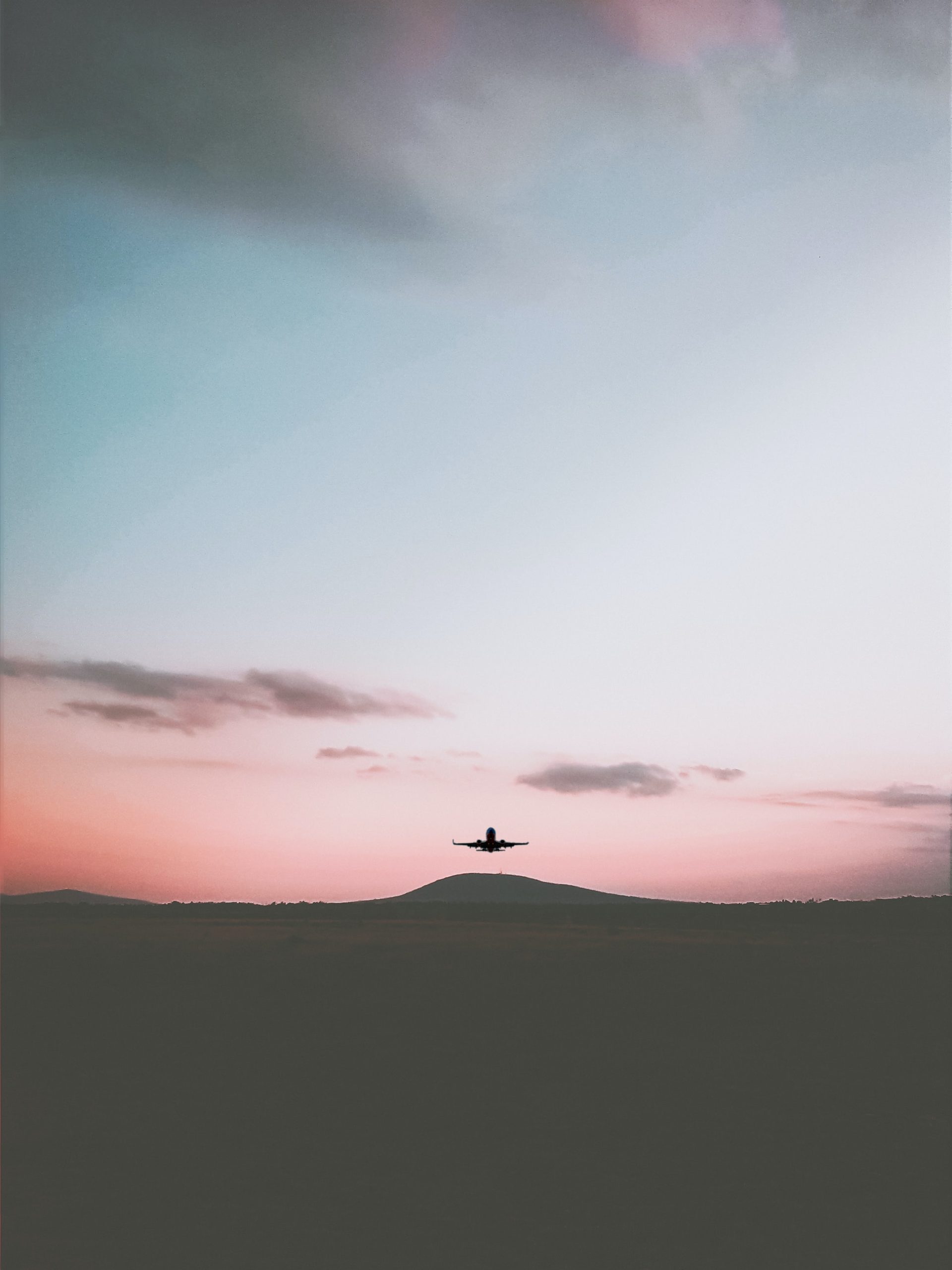 Silhouette of an airplane flying under cloudy sky during daytime